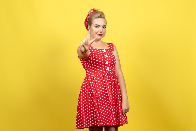 young female in red polka dot dress posing on yellow