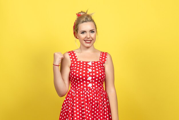 young female in red polka dot dress posing on yellow