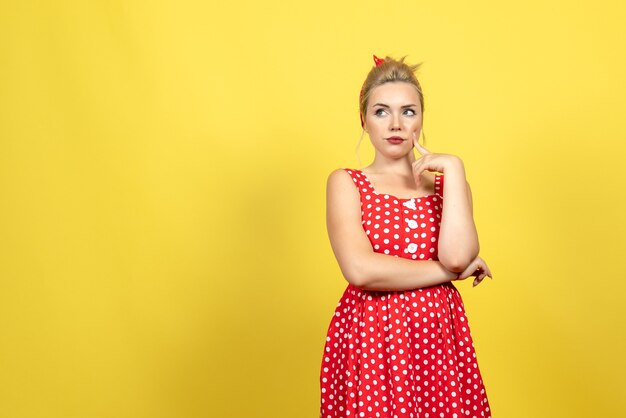 young female in red polka dot dress posing on yellow