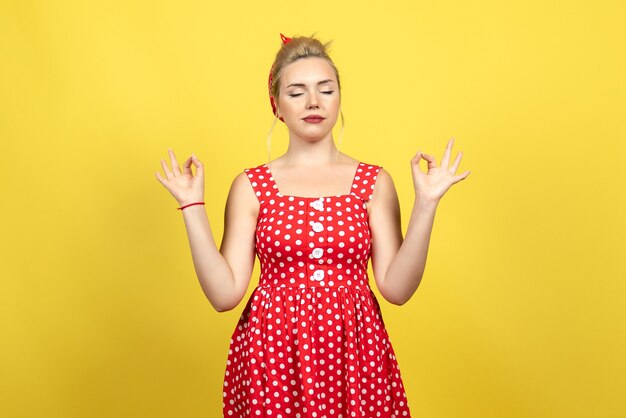 young female in red polka dot dress posing on yellow