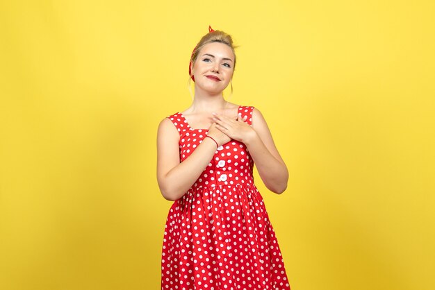 young female in red polka dot dress posing on yellow