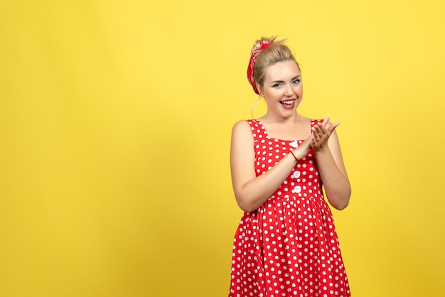 young female in red polka dot dress posing on yellow