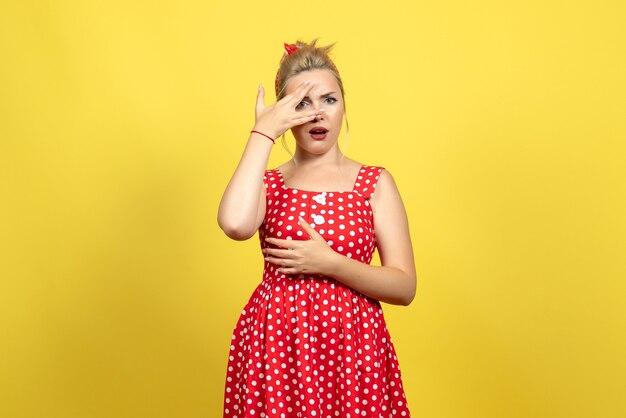 young female in red polka dot dress posing on yellow