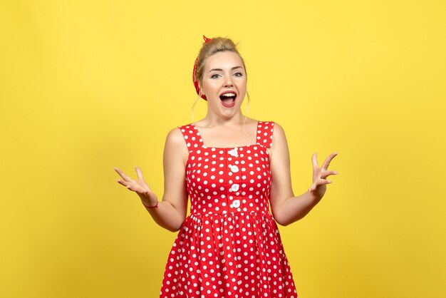 young female in red polka dot dress posing on yellow