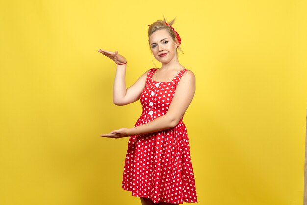 young female in red polka dot dress posing on yellow