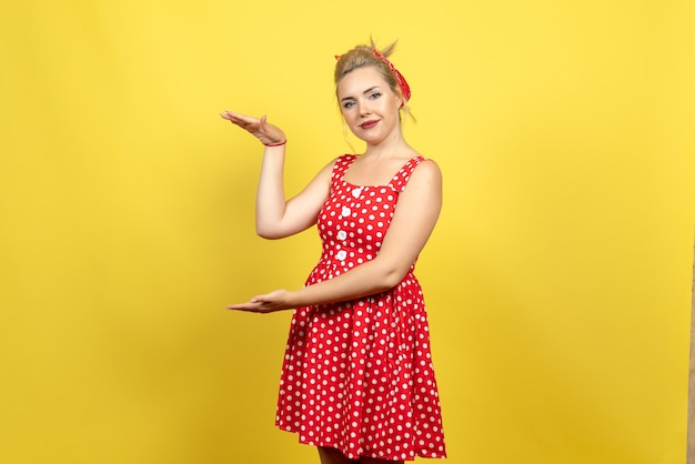 young female in red polka dot dress posing on yellow