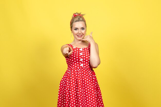 young female in red polka dot dress posing on yellow