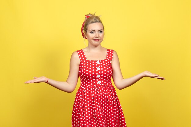 young female in red polka dot dress posing on yellow