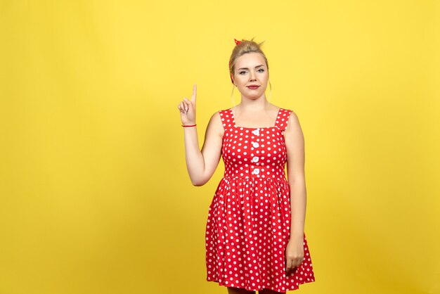 young female in red polka dot dress raising her finger on yellow