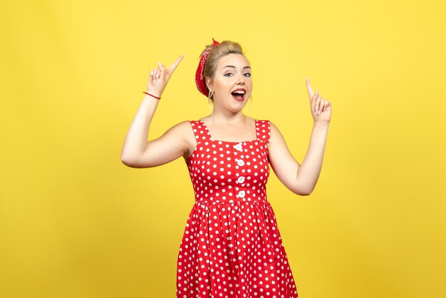young female in red polka dot dress raising her fingers on yellow