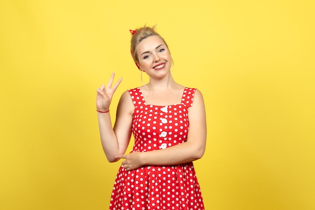 young female in red polka dot dress smiling and posing on yellow