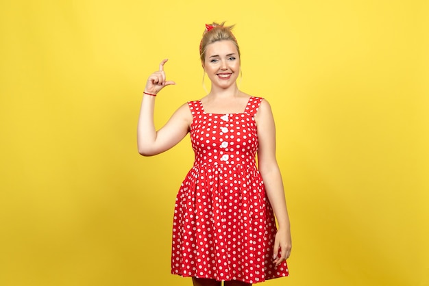 Free photo young female in red polka dot dress smiling on yellow