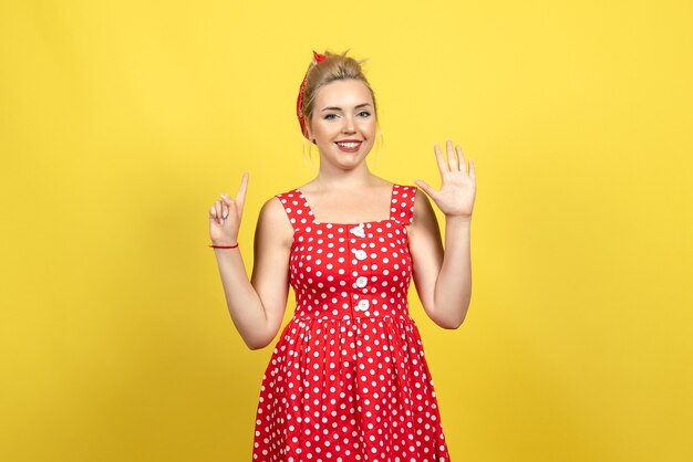 young female in red polka dot dress smiling on yellow