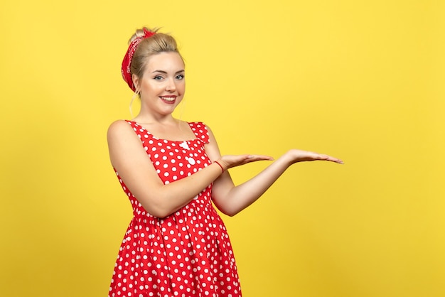 young female in red polka dot dress smiling on yellow