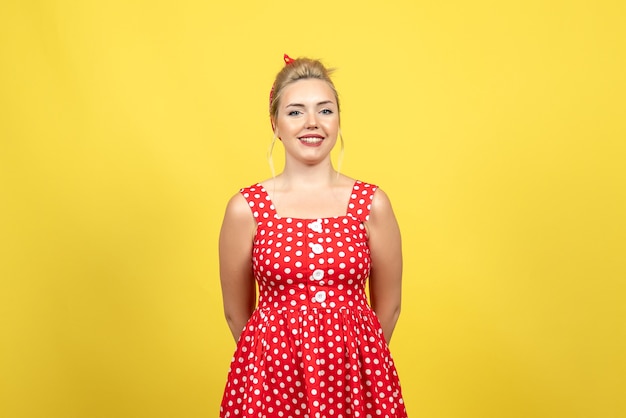 молодая женщина в красном платье в горошек стоит и улыбается на желтом