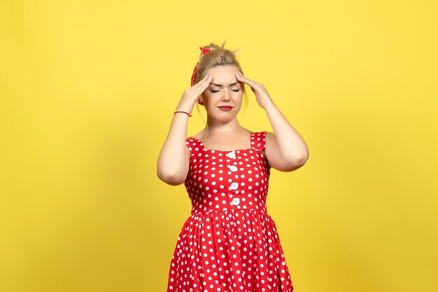 黄色の頭痛に苦しんでいる赤い水玉模様のドレスの若い女性