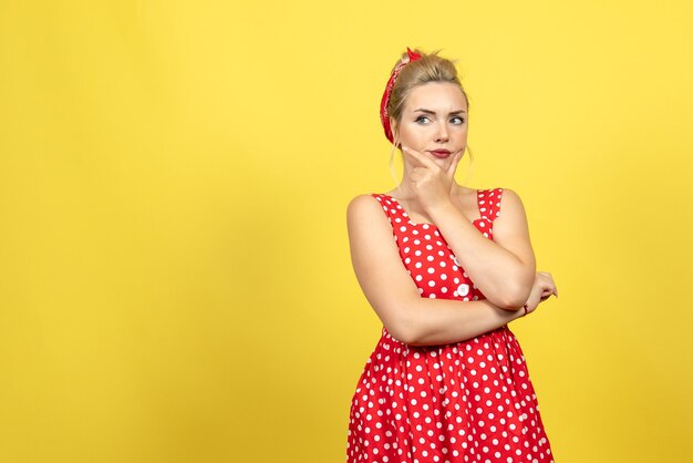 Free photo young female in red polka dot dress thinking on yellow