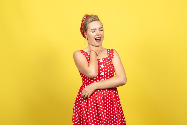 young female in red polka dot dress touching her throat on yellow