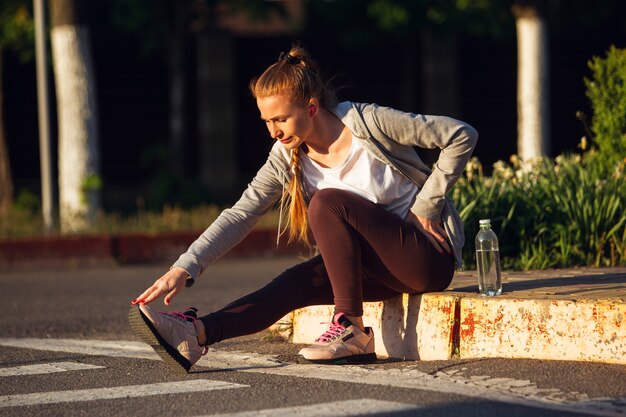 若い女性ランナー、アスリートは日差しの中で街の通りでジョギングしています。