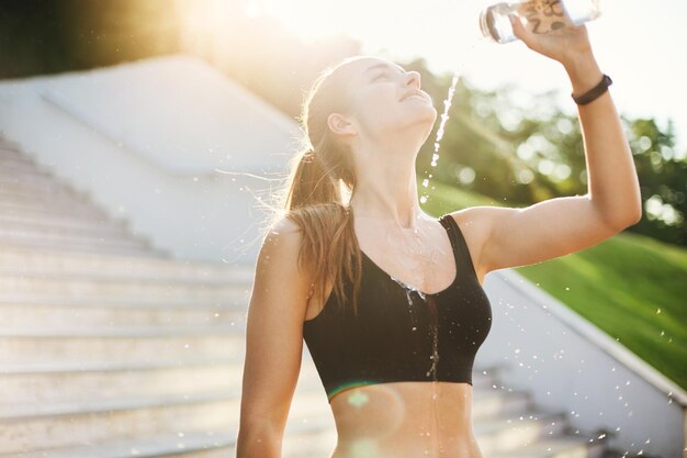 Молодая бегунья обливает себя водой после долгой и тяжелой утренней тренировки Концепция городского спорта и образа жизни
