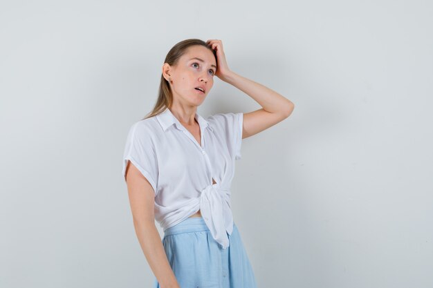 Young female scratching head in blouse and skirt and looking pensive