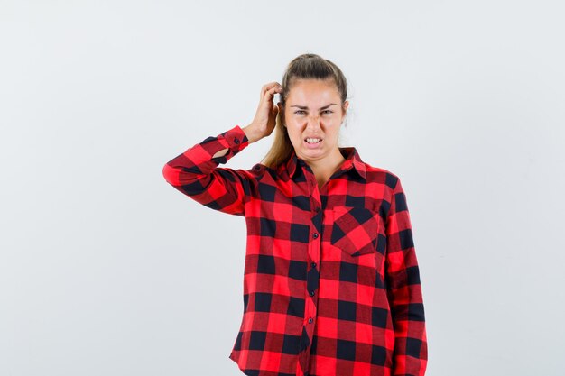Young female scratching head in checked shirt and looking pensive , front view.