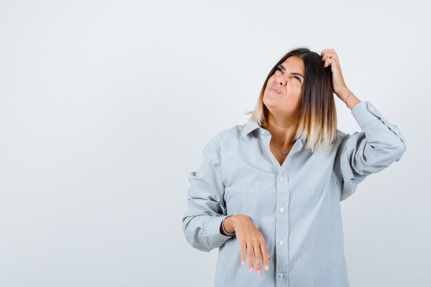 Young female scratching head in oversized shirt and looking thoughtful. front view.