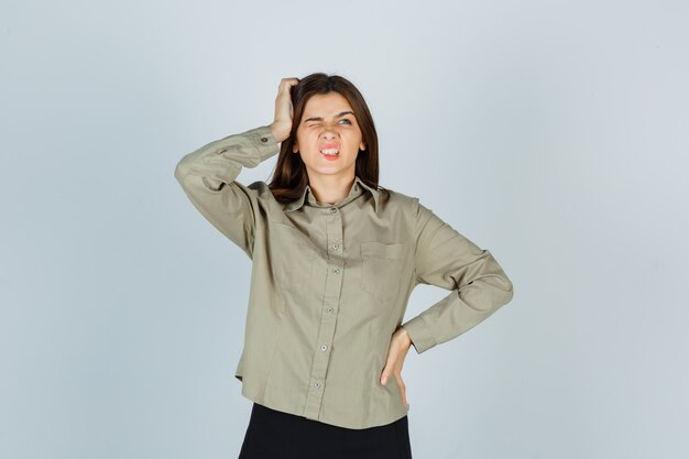 Young female scratching head while frowning in shirt and looking forgetful