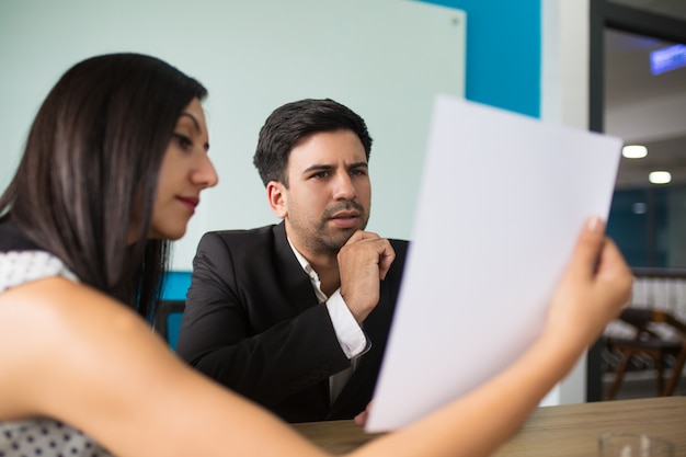 Young female secretary showing document to puzzled executive