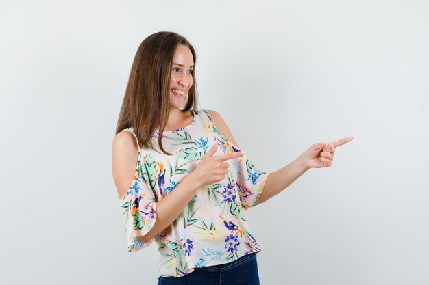 Young female in shirt, jeans pointing to side and looking cheery , front view.