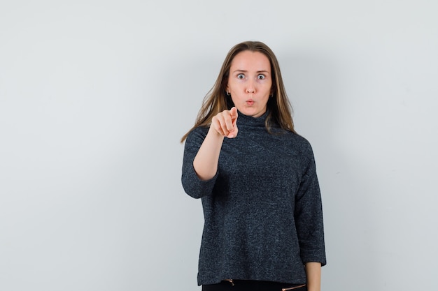 Young female in shirt pointing at camera and looking surprised 