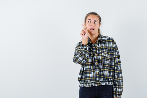 シャツを着た若い女性、指を上に向けて物思いにふけるショーツ、正面図。