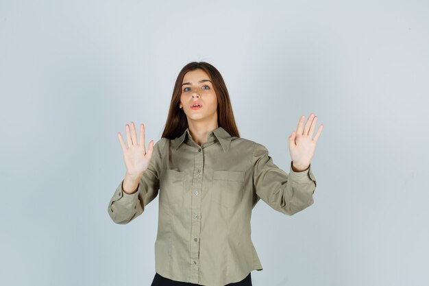 Молодая женщина в рубашке показывает жест стоп и выглядит испуганной, вид спереди.