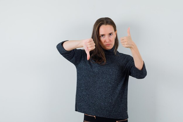 Young female in shirt showing thumbs up and down and looking hesitant 