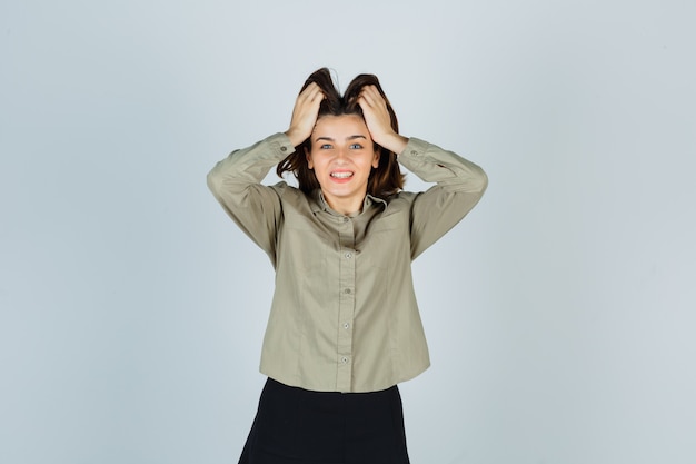 Foto gratuita giovane donna in camicia, gonna stringendo la testa con le mani e guardando felice