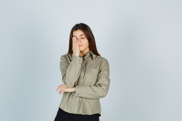 Young female in shirt, skirt holding hand on eye and looking fatigued