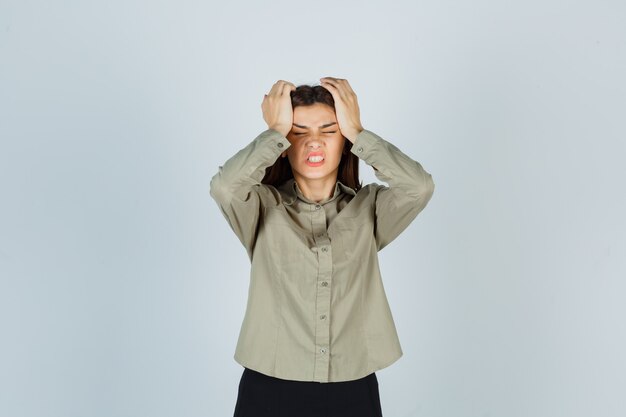 Young female in shirt, skirt keeping hands on head and looking annoyed , front view.