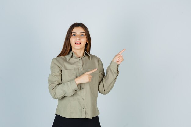 Young female in shirt, skirt pointing at upper right corner and looking wondered