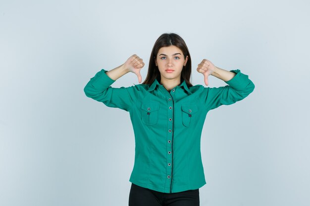 緑のシャツを着て二重の親指を示し、不機嫌そうに見える若い女性、正面図。