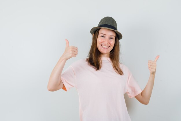 Young female showing double thumbs up in pink t-shirt, hat and looking glad , front view.