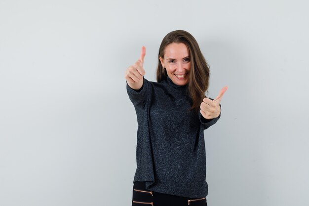 Young female showing double thumbs up in shirt and looking merry. front view.