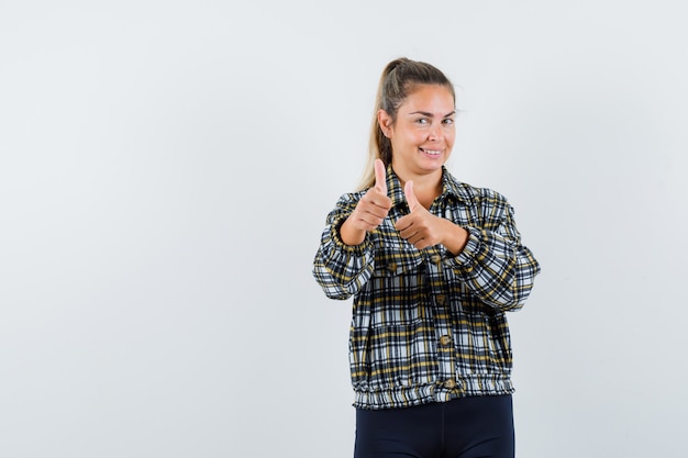 Young female showing double thumbs up in shirt, shorts and looking confident. front view.