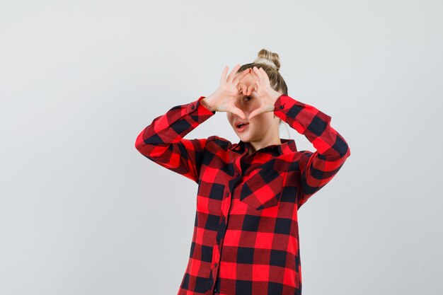 Foto gratuita giovane femmina che mostra il gesto del cuore in camicia controllata e guardando fiducioso, vista frontale.