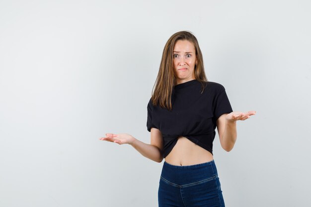 Young female showing helpless gesture in black blouse, pants and looking confused