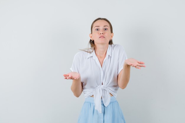 Young female showing helpless gesture in blouse and skirt and looking confused