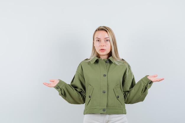 Young female showing helpless gesture in green jacket and looking displeased. front view.