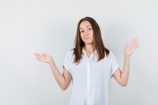 Young female showing helpless gesture in white blouse and looking puzzled