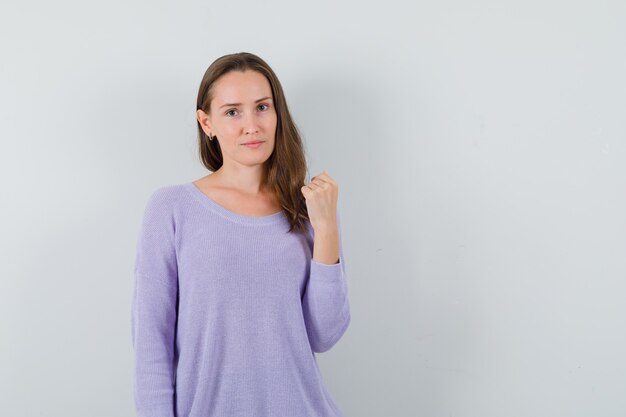 Young female showing her fist in lilac blouse and looking powerful. front view. space for text
