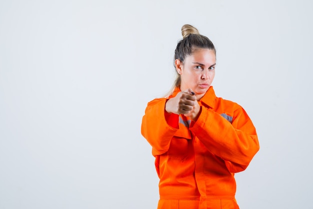 Giovane donna che mostra il suo pugno in uniforme da lavoro e dall'aspetto aggressivo. vista frontale.