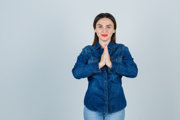 Young female showing namaste gesture in denim shirt and jeans and looking peaceful
